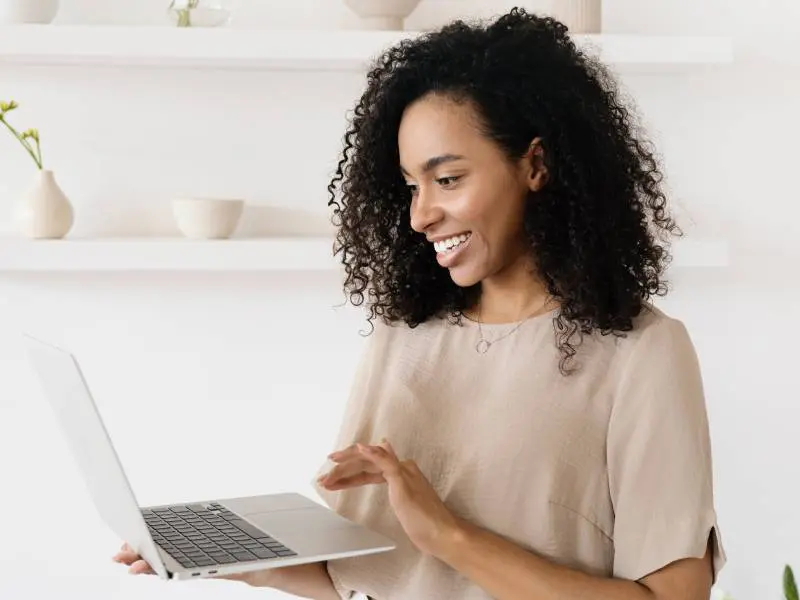 A woman is smiling while looking at her laptop.