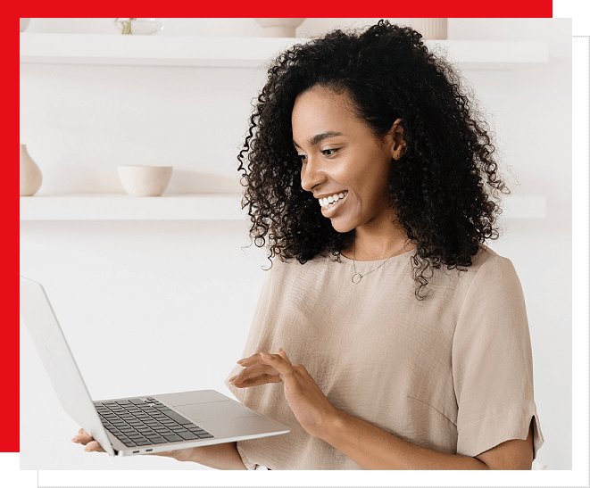 A woman is smiling while using her laptop.